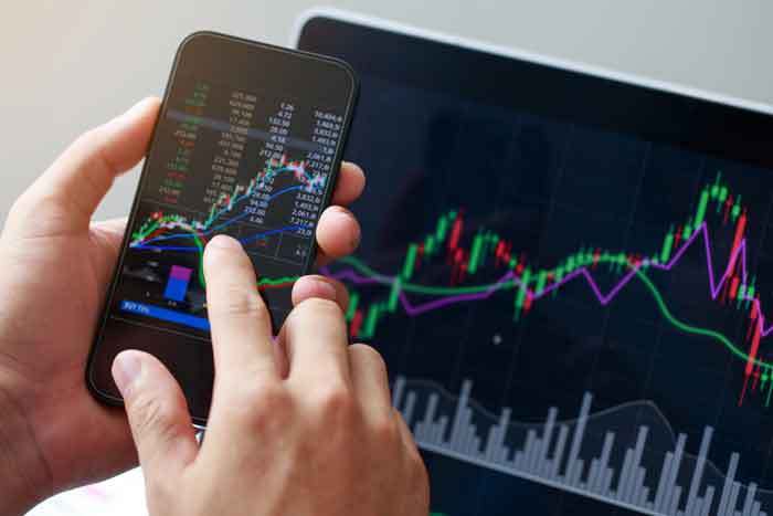 Hand holding phone with market charts displayed